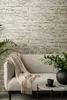 A sofa with a throw blanket and a coffee table with a vase and a cup in front of a stone-patterned wall. Produktbild-Vorschau