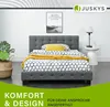 A bedroom scene featuring a bed, a nightstand with a lamp, and a plant. Náhled obrázku produktu