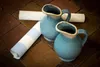 Two blue ceramic pitchers and two rolls of wallpaper are placed on a brick-like floor. Produktbild-Vorschau