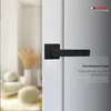A black door handle on a white door with a blurred background of a room interior. Produktbild-Vorschau