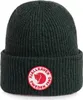 A close-up studio shot of a dark green knitted beanie with a circular red and white logo patch on the front. Anteprima dell’immagine prodotto