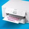 A white Epson printer is shown printing a sheet of paper with pink text on a blue background. Náhľad obrázku produktu