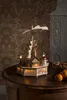 A wooden Christmas pyramid with LED lights sits on a wooden table next to a bowl of cookies and tangerines. Produktbild-Vorschau