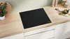 A black induction hob is shown on a light wood countertop in a modern kitchen setting. Voir les images du produit