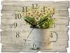 A wall clock with a floral design of daisies in a pitcher, set against a rustic wooden background with handwritten script. Produktbild-Vorschau
