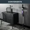 A cordless vacuum cleaner is shown charging on a wall mount next to a black cabinet with decorative items on top. Voir les images du produit