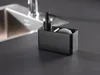 A black soap dispenser with a sponge holder sits on a dark countertop next to a sink. Produktbild-Vorschau