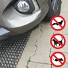 A close-up view of a car's bumper and tire resting on a black plastic grid placed on a paved surface. Three circular red and white signs with animal silhouettes are visible on the right side of the image. Náhľad obrázku produktu