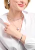 A woman wearing a white shirt and silver jewelry, including earrings, a necklace with a pendant, and a bracelet. Produktbild-Vorschau