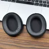 Two black ear pads are placed on a wooden surface in front of a laptop. Podgląd zdjęcia produktu