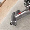 A close-up view of a vacuum cleaner attachment on a carpeted surface next to a wooden surface. Produktbild-Vorschau
