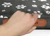 A hand is holding a brown leather tag attached to a dog bed with paw print patterns. Produktbild-Vorschau