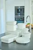 A collection of white plastic food storage containers with transparent lids are neatly arranged on a dark countertop in a modern kitchen. Produktbild-Vorschau