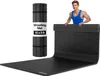 A man is standing behind a black wrestling mat that is unrolled on a white background. A rolled-up wrestling mat is also visible. Podgląd zdjęcia produktu