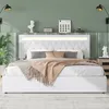 A white upholstered bed with a tufted headboard and LED lighting is shown in a bedroom setting with green walls and decorative items on a shelf above. Náhľad obrázku produktu