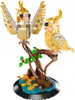 A detailed model of two gold cockatiels perched on a tree branch, with a base depicting water and autumn leaves. Náhľad obrázku produktu