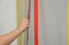 A hand is holding a red zipper with a purple strip on it, against a background of vertical stripes. Produktbild-Vorschau