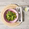 A salad is served on a pink plate on a woven placemat, with a fork and a glass of water with a lime slice. Náhled obrázku produktu