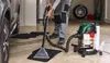 A person is using a wet vacuum cleaner to clean car mats in a garage. Produktbild-Vorschau