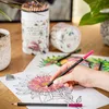 A hand coloring a flower in a coloring book with colored pencils. Produktbild-Vorschau