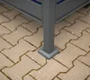 Close-up of the base of a gray metal structure, possibly a trash can enclosure, resting on interlocking tan pavers. Náhled obrázku produktu