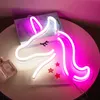 A neon unicorn light is displayed on a table next to a book and a perfume bottle. Náhled obrázku produktu