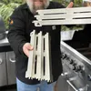 A man is holding grill parts in front of a grill. Produktbild-Vorschau