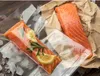 Two salmon fillets, one vacuum-sealed with lemon and rosemary, are displayed on a surface with ice. Anteprima dell’immagine prodotto