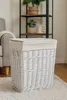 A white wicker laundry basket with a beige fabric liner and lid sits on a rug in a room. Produktbild-Vorschau
