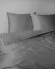 A close-up view of a grey duvet cover and pillowcases with white piping. Náhled obrázku produktu