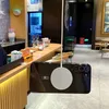 A smartphone with a magnetic charging ring attached is suspended in front of a cafe counter. Náhled obrázku produktu