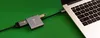 A USB-C adapter hub is connected to a laptop, with a green background. Produktbild-Vorschau