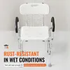 A white shower chair with armrests and a backrest, shown in a bathroom setting with water droplets simulating a shower. Podgląd zdjęcia produktu