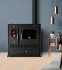 A black wood-burning stove with a glass oven door and a visible fire in the left compartment, set against a blue wall and on a light wood floor. Produktbild-Vorschau