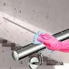 A hand wearing a pink glove is cleaning a stainless steel handrail with a blue cloth, with a staircase and water droplets in the background. Produktbild-Vorschau
