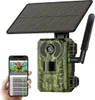 A hand holds a smartphone displaying a live feed from a trail camera, which is also shown in the image. The trail camera is mounted on a solar panel. Produktbild-Vorschau