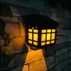 A solar wall light with a flame effect is mounted on a stone wall at night, casting a warm yellow light. Podgląd zdjęcia produktu