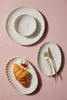 A top-down view of white ceramic plates and cutlery arranged on a pink background. Produktbild-Vorschau