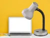 A desk lamp is positioned next to a laptop on a white surface, with a textured yellow background. Anteprima dell’immagine prodotto