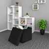A black storage ottoman is open and filled with cushions, placed on a grey carpet in front of white bookshelves. A potted green plant sits to the right. Produktbild-Vorschau