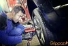 A mechanic in a garage is using a power tool to tighten a lug nut on a car tire. Produktbild-Vorschau