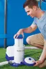 A man is shown kneeling next to a pool filter pump, appearing to be performing maintenance or setup. Voir les images du produit