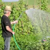 A man watering plants in a garden with a hose. Produktbild-Vorschau