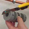 A hand is holding a piece of foam pipe insulation while a utility knife is cutting it. A copper pipe is visible in the background. Produktbild-Vorschau