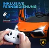 A person holding a remote control for an orange electric toy car with its doors open, set against a dark, city-like background. Produktbild-Vorschau