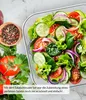 A close-up of a salad in a clear bowl, with ingredients like tomatoes, cucumbers, and red onions, along with a bowl of peppercorns and fresh parsley and tomatoes in the foreground. Produktbild-Vorschau
