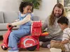 A father and his two children are playing with a Play-Doh pizza delivery scooter set in a living room. Produktbild-Vorschau