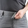 Close-up of a person's hand adjusting the waistband of gray pants, showing a Velcro closure. Náhled obrázku produktu