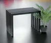 A black metal bench with a slatted design sits next to a potted plant on a reflective black surface. Produktbild-Vorschau