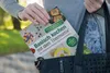 A person is placing a cookbook into a black tote bag. Produktbild-Vorschau